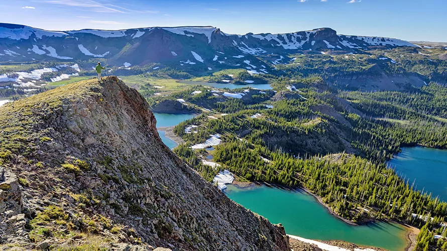 Landscape from high up in Rocky Mountains in the Flattops Wilderness Area of Colorado with man traversing along ridge on summer day with alpine lakes below and background. Stunning mountain view.
