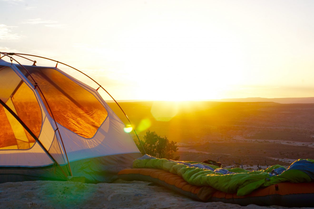 A tent and sleeping bag on a rock during sunset at Arches National Park. 