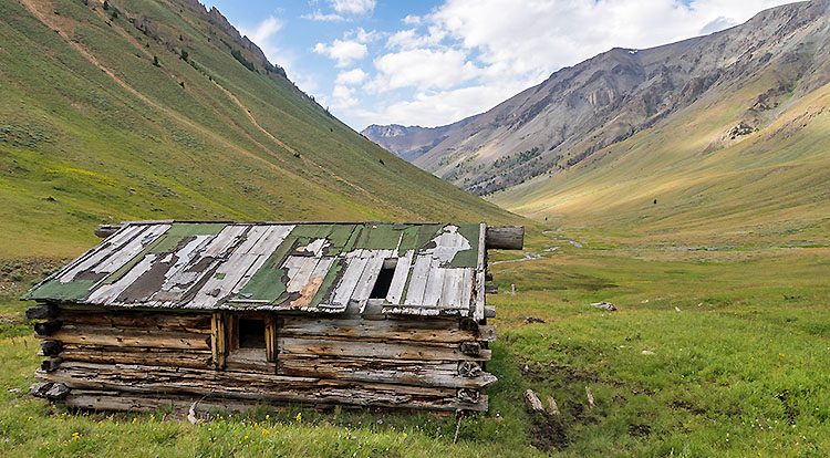 Old wooden shack in grassy field near hills