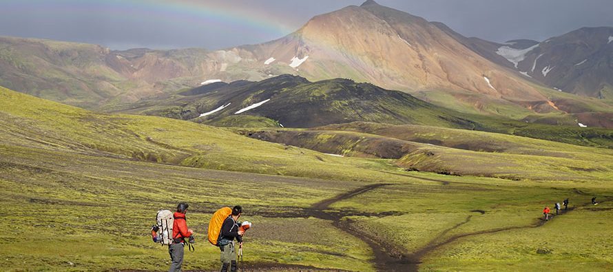 Two hikers walking over expanse of green grassy mountains