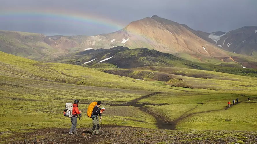 Two hikers walking over expanse of green grassy mountains