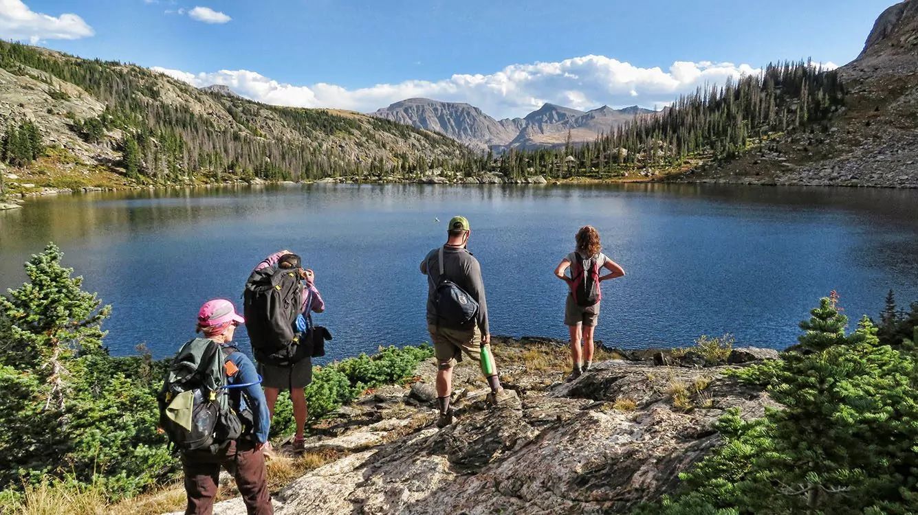 Hikers standing by lake with mountains