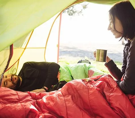 Two friend traveling and spending time in tent while drinking coffee in the morning. Happy people in camping. View from inside. Couple of travelers