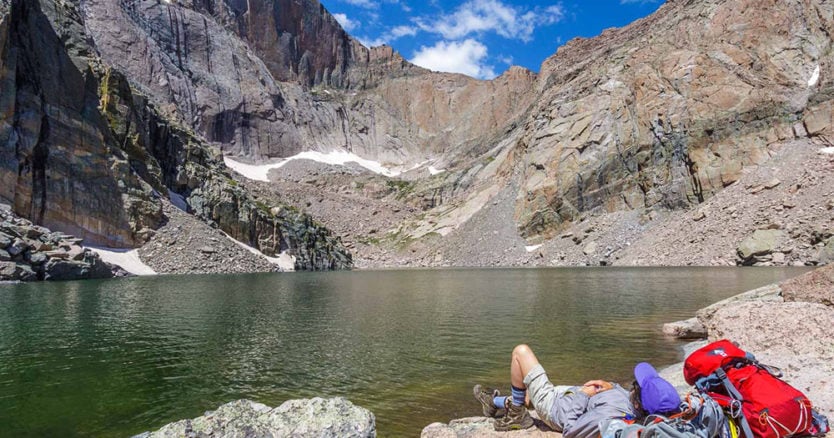 A hiker relaxes at the summit near an alpine lake in Rocky Mountain National Park