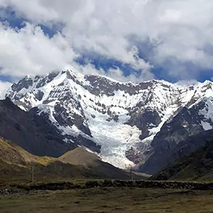 Blue skies are spotted with thick clouds over snowy Peruvian mountains