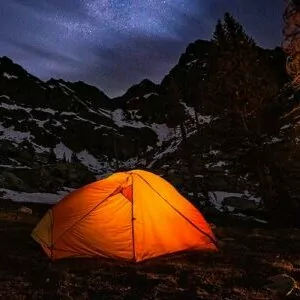 an orange tent lights up during a dark night of alpine camping
