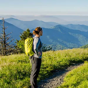 A hiker looks out at the the Great Smoky Mountains from a lush trail