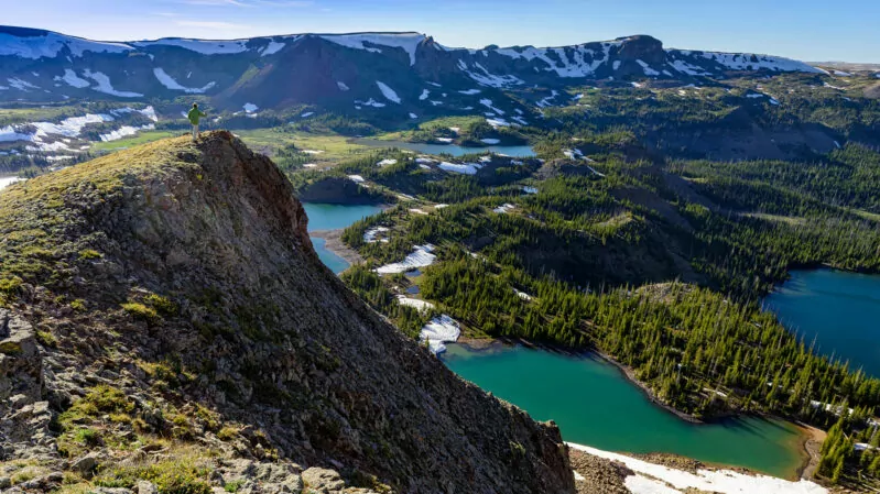 Landscape from high up in Rocky Mountains in the Flattops Wilderness Area of Colorado with man traversing along ridge on summer day with alpine lakes below and background. Stunning mountain view.