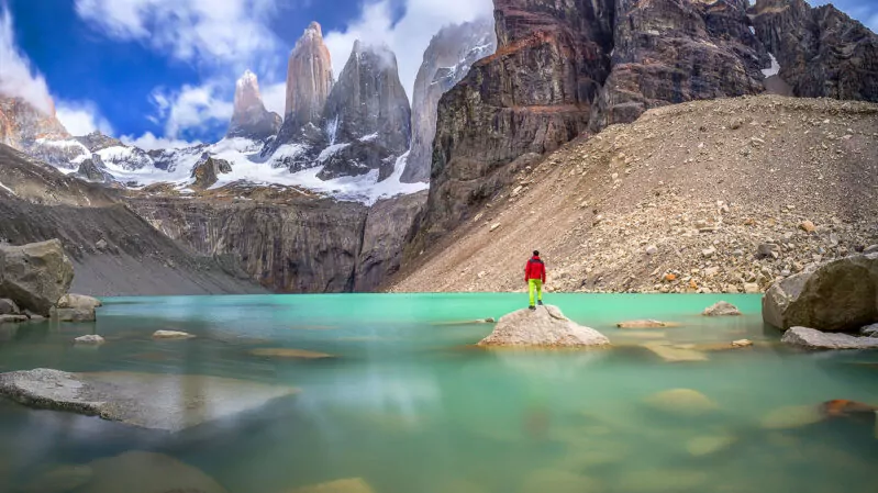 Hiker in red jacket admiring 3 peaks at Base de las Torres viewpoint in Torres del Paine, Patagonia