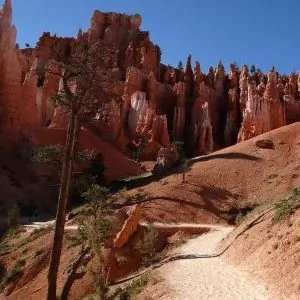 Crimson colored rock formations reach up towards the sky as a trail aims to approach them.