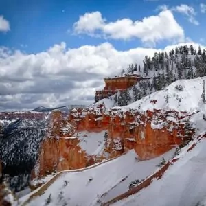 Blue skies spotted by puffy clouds sit above the snow covered canyons of Bryce Canyon.