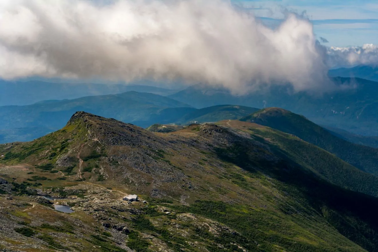 A vista of the White Mountains of New Hampshire from the summit of Mount Washington, the hut at Lake of the Clouds on the ridge.