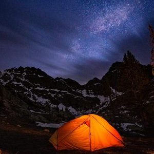 A tent lights up from the inside during a dark starry night in Rocky Mountain National Park