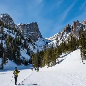 A snowshoer treks onwards higher into the mountains in Rocky Mountain National Park with blue skies
