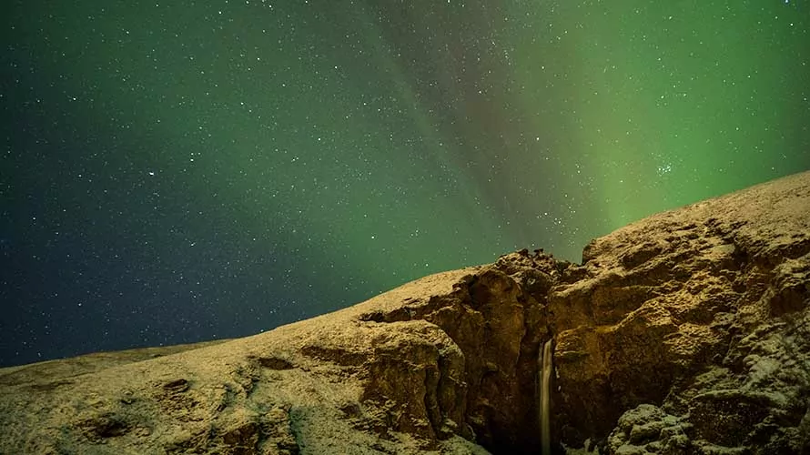 An Iceland waterfall lit up by the Aurora Borealis