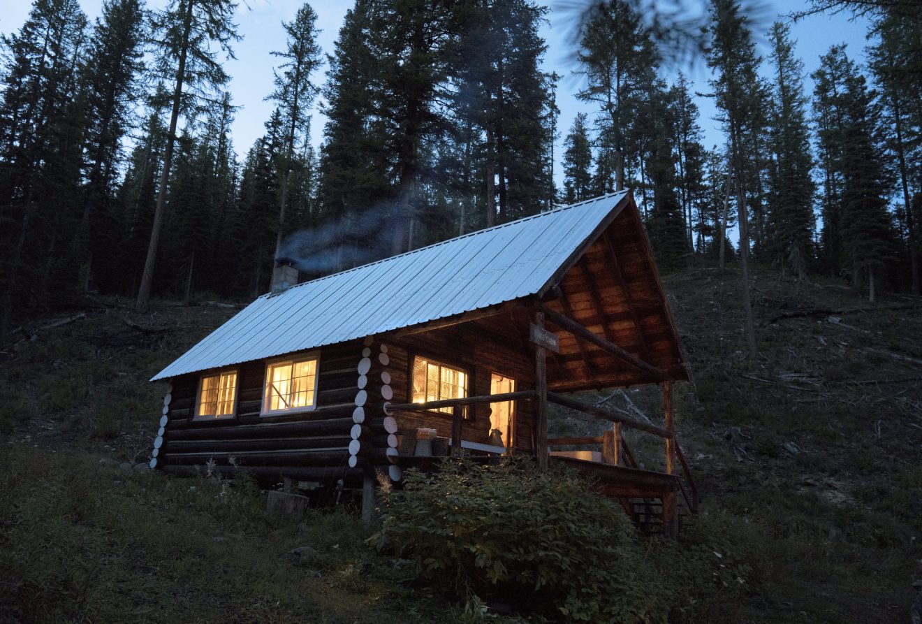 Interior lights illuminate Ninko Cabin, a backcounty hut, at dusk in Montana. 