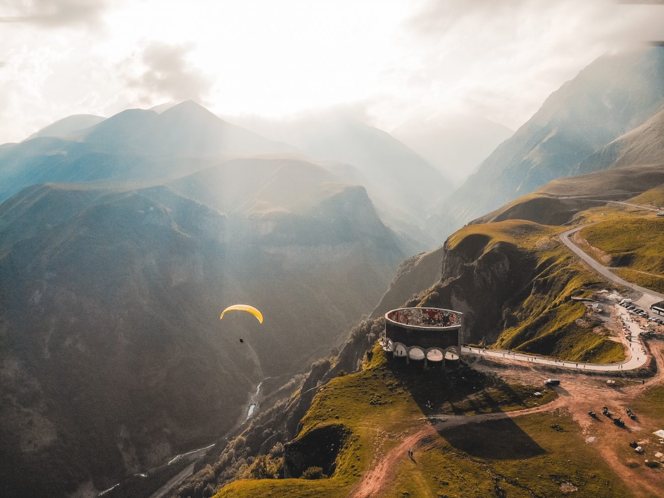 A yellow paraglider hovers over the ridgeline in the Caucaus Mountains in Georgia, a perfect adventure vacation destination. 