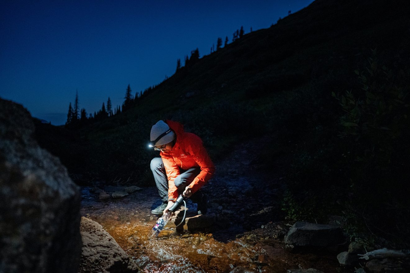 Man filters water by headlamp light while backpacking