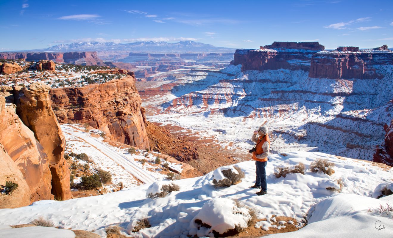 A man with a camera stands in a snowy landscape in Canyonlands