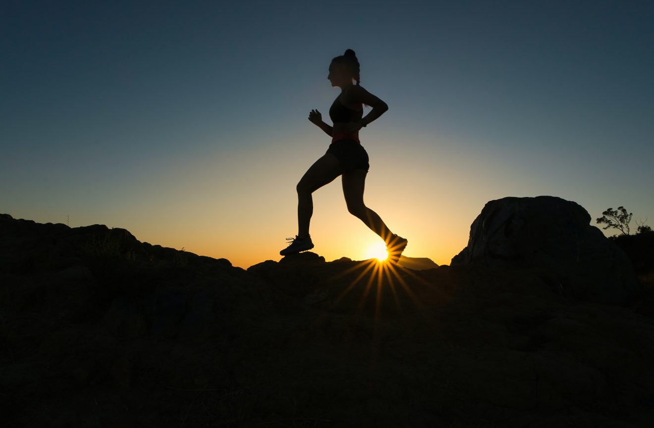 woman silhouetted by the setting sun while training for backpacking on a rocky ridge