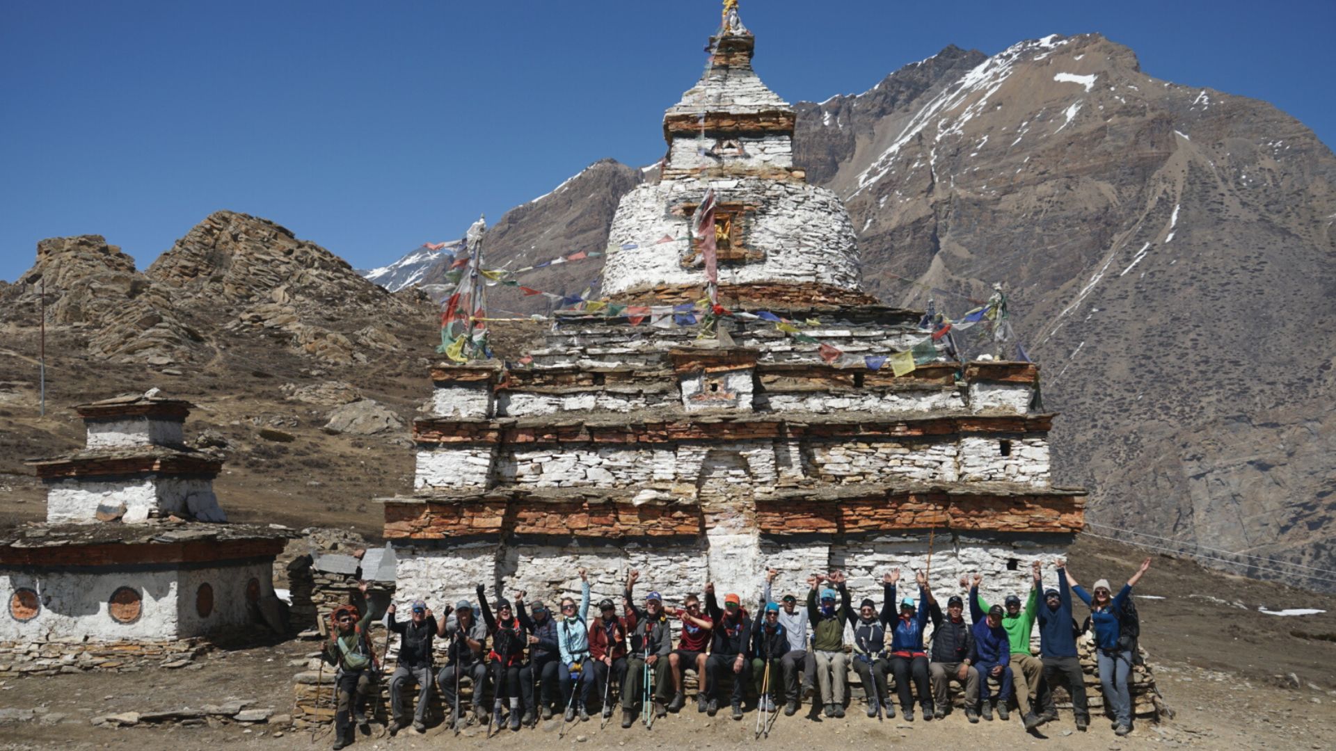 A large group poses in front of a traditional Nepalese structure in the mountains