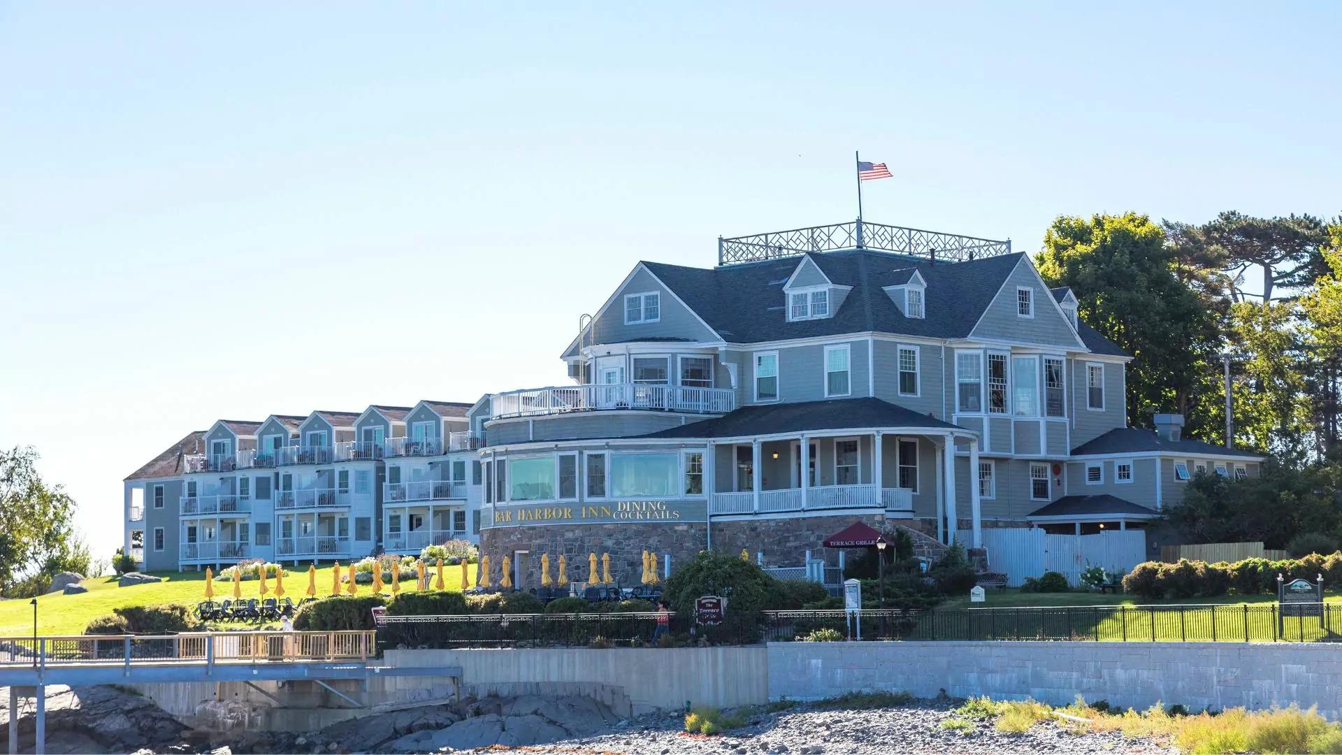 Historic Bar Harbor Inn pictured sitting on the rocky Maine coastline on a sunny day