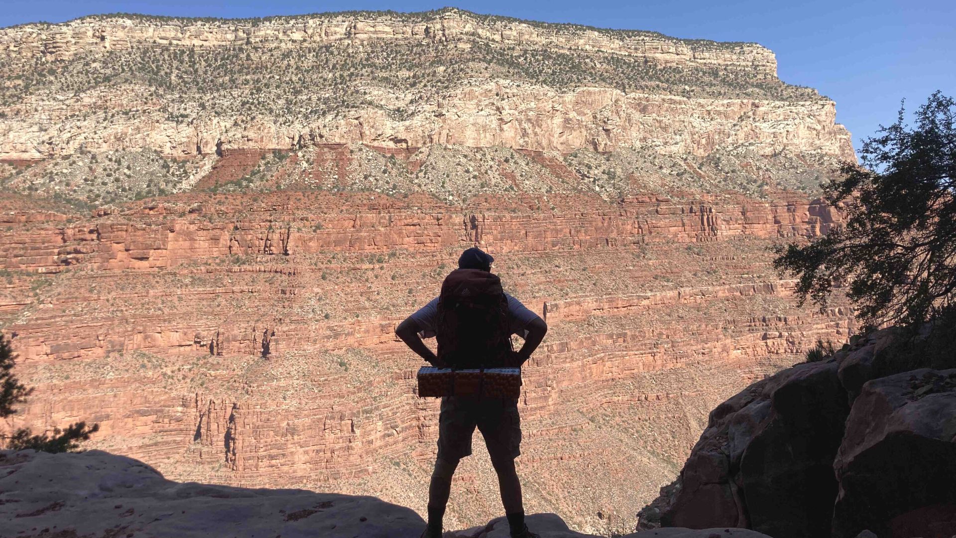 Backpacker stands with back to camera and hands on hips looking out at the Grand Canyon