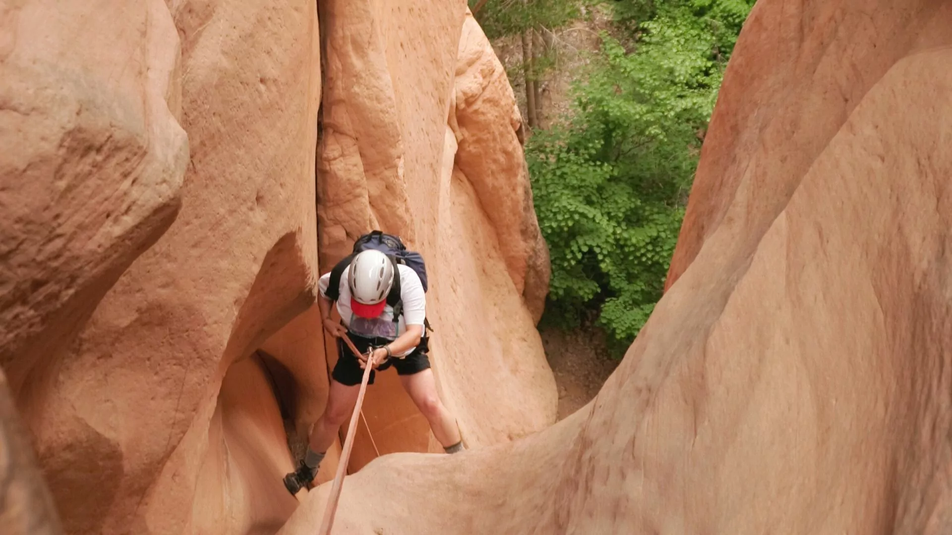 A canyoneer rappels between sandstone walls