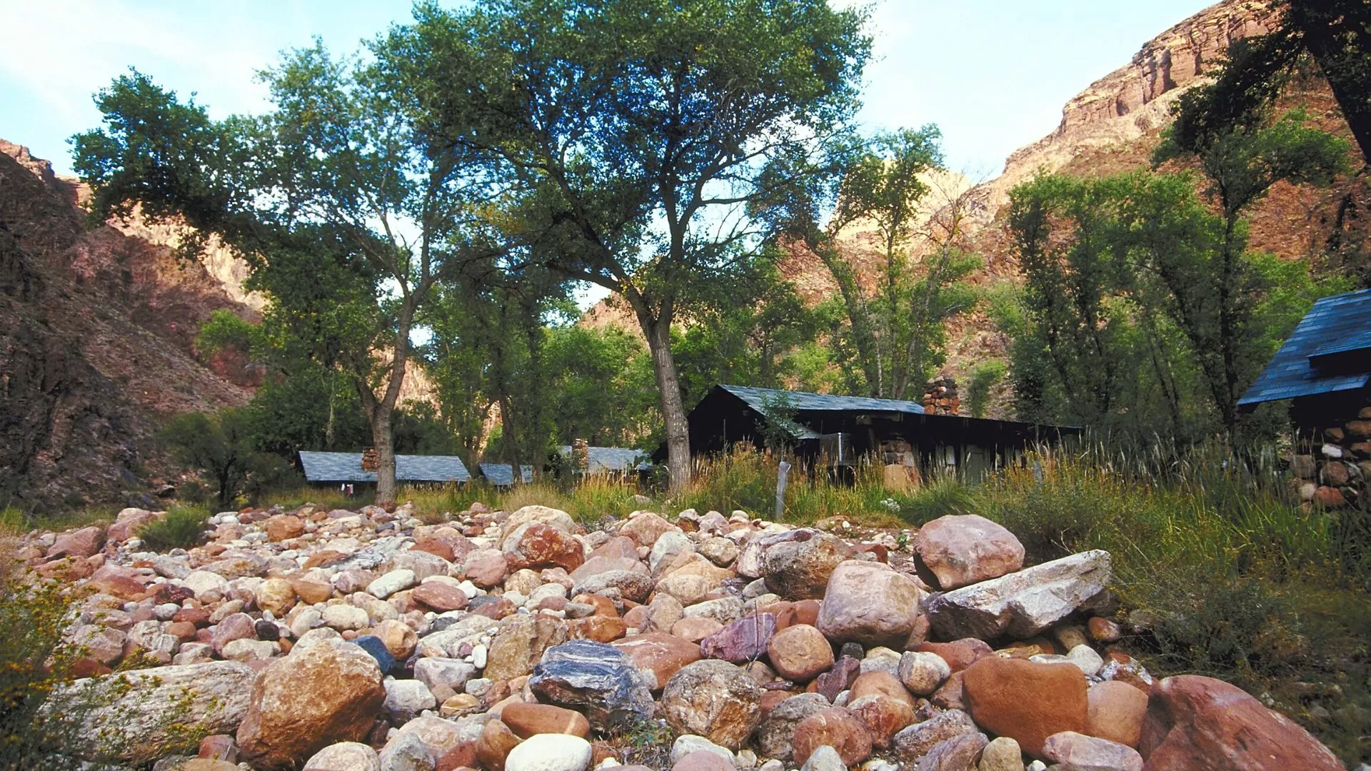 Rustic log cabins sit shaded by trees at the bottom of the Grand Canyon