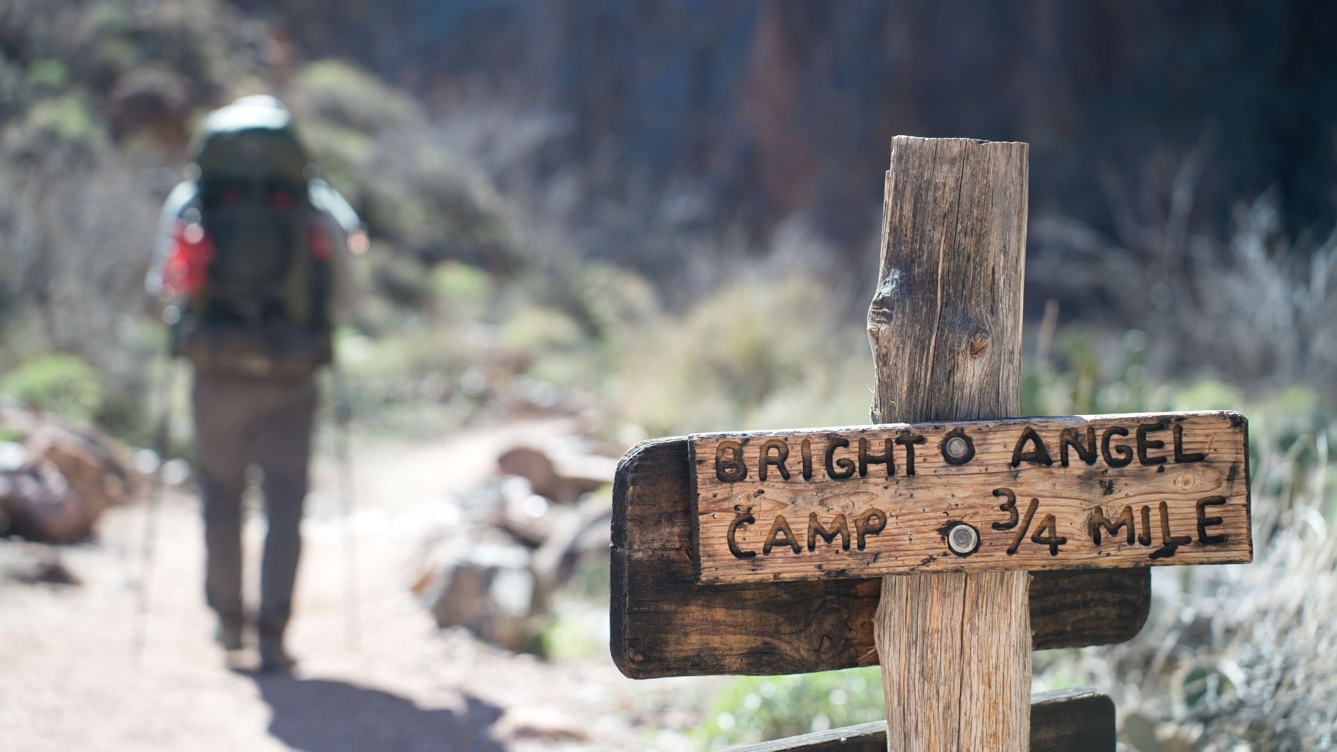 In the right foreground a wooden signpost reads "Bright Angel Campground," while a backpacker hikes past to the left