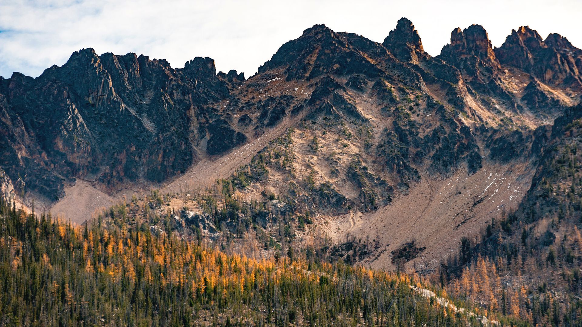 Rocky mountain slopes rise high above an autumnal colored forest 