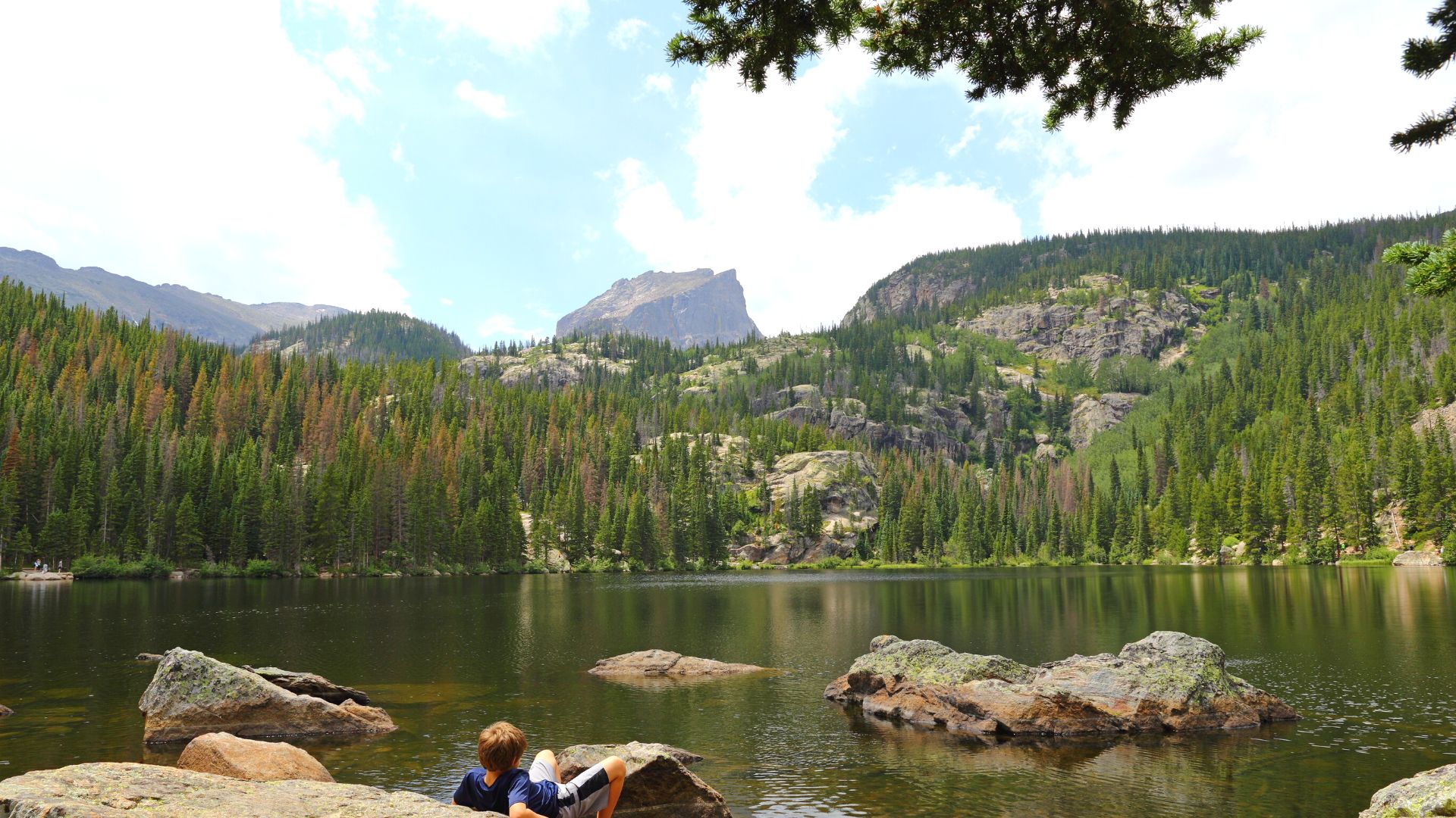 Someone reclines on a rock at the edge of a clear, still lake in the mountains