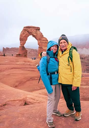 Two hikers hugging in front of Delicate Arch, Arches National Park