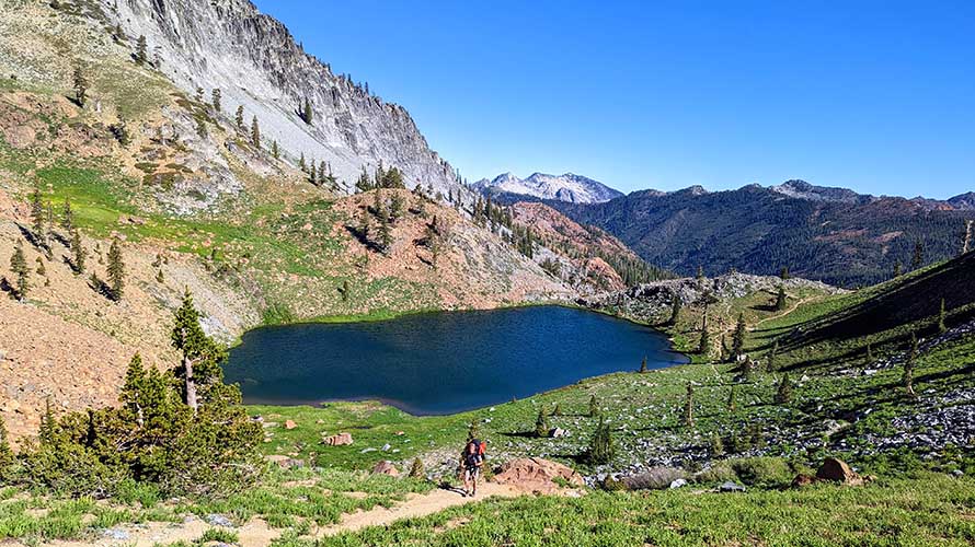 Backpacker hiking on trail by alpine lake in Trinity Alps Wilderness, California