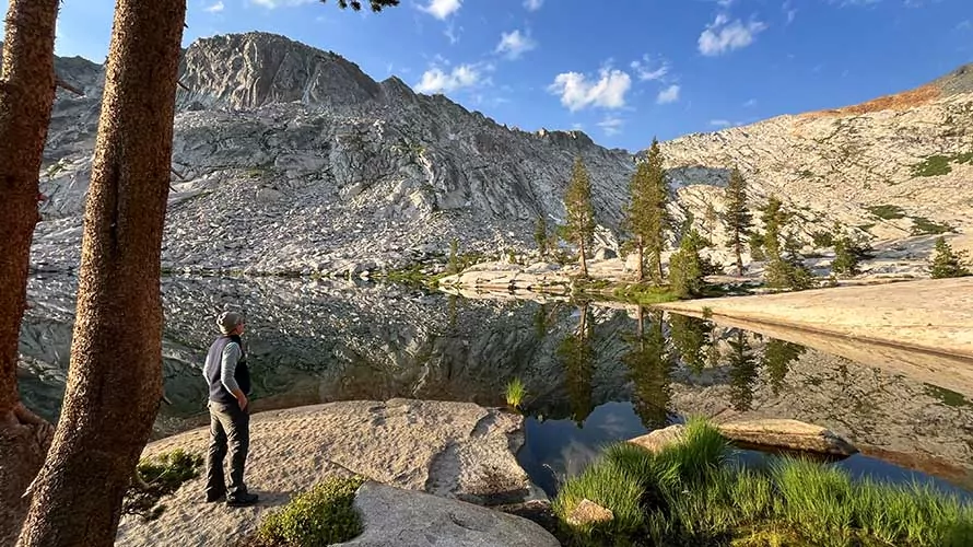 A lone hiker at sunrise enjoying the view of a gorgeous alpine lake in the Sierra