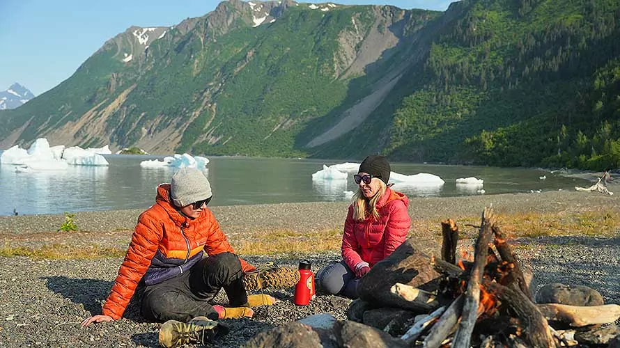 Backpacking group sitting next to a campfire on a beach in Kenai