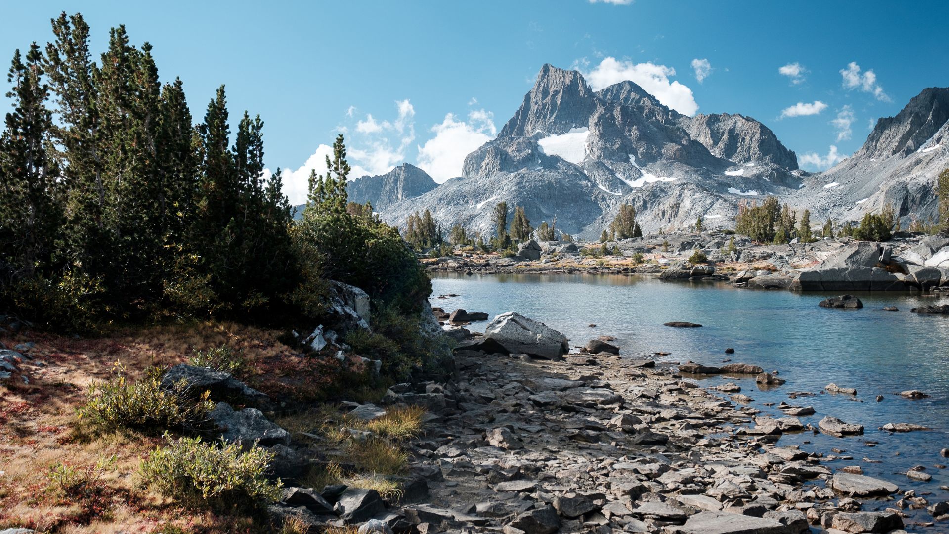 A jagged snowy peak in the high Sierra stands behind a pristine alpine lake