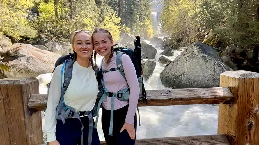 Two women standing on a bridge over a thundering river in Yosemite National Park