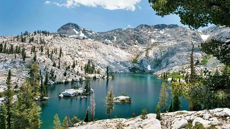 Hiker standing on the shores of an alpine lake in the Sierra Nevada Mountains