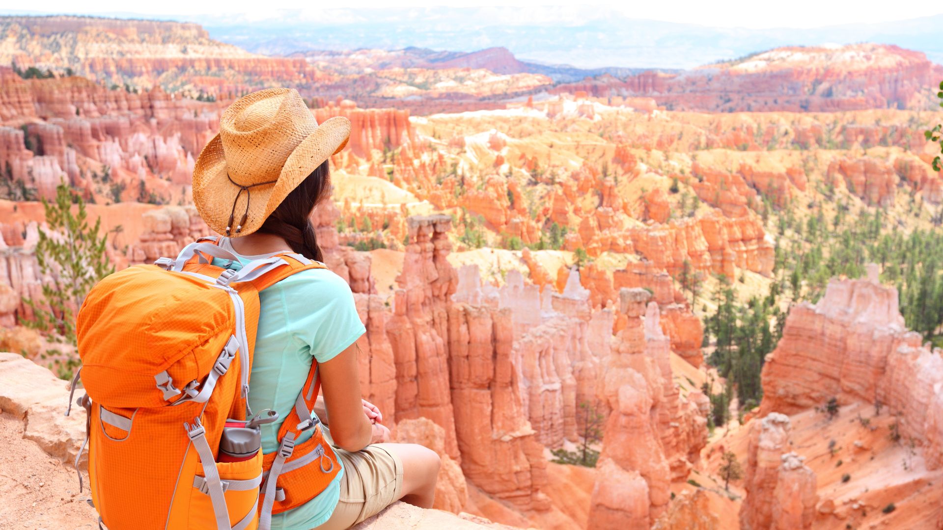 A hiker with a daypack on sits looking out at the bryce canyon hoodoos