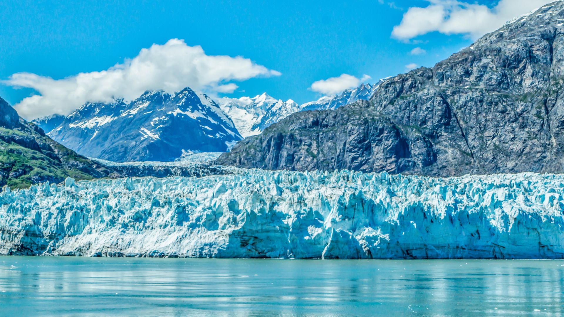 A glacier meets the ocean while rugged mountains rise behind in Glacier Bay National Park, Alaska