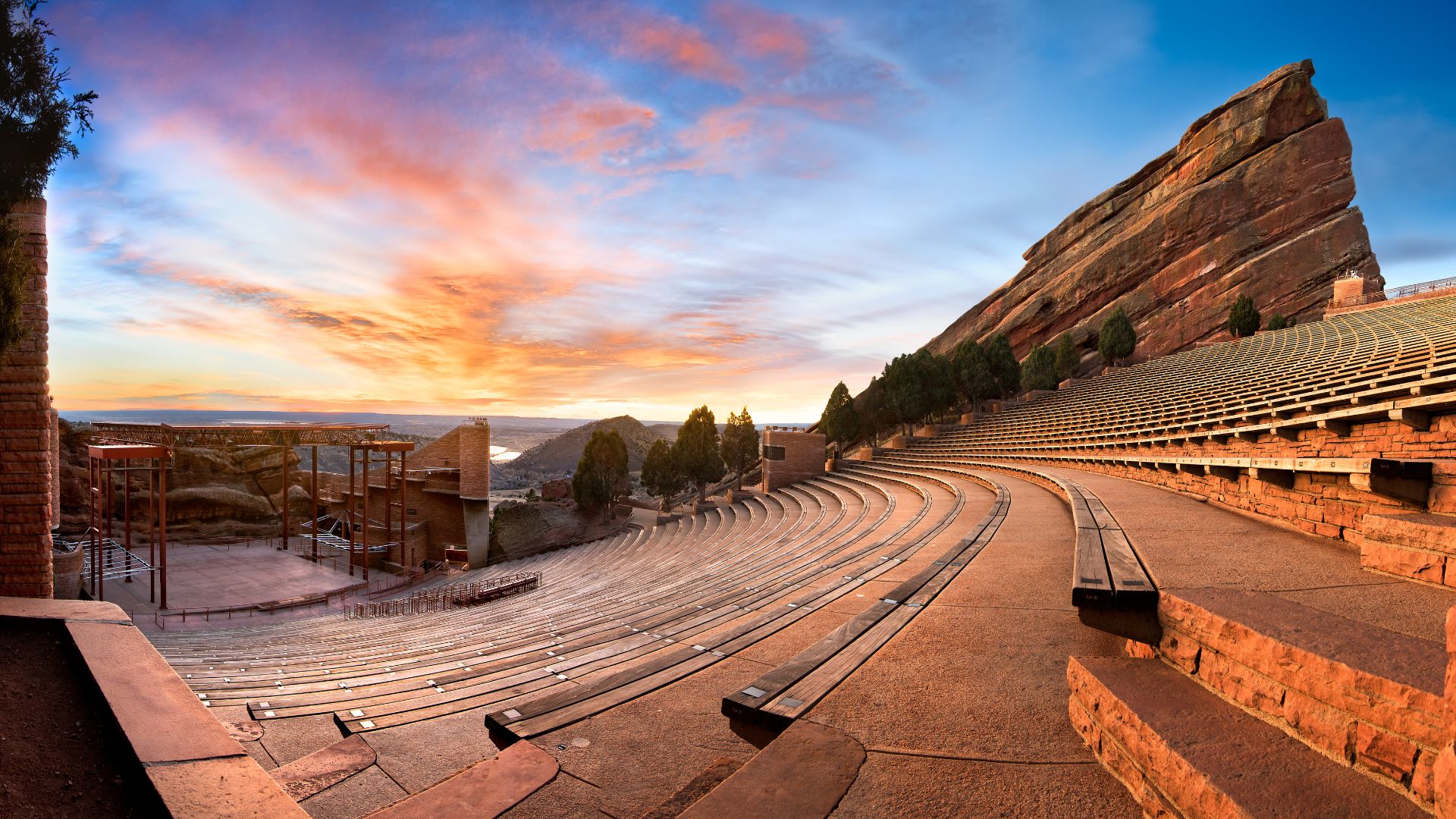 The terraced seats of red rock amphiteater concert venue in Colorado are arrayed under a orange sunset sky