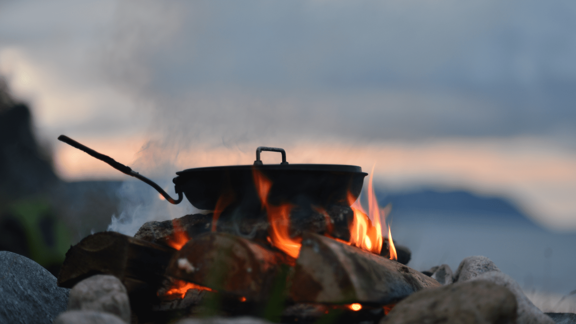 A frying pan simmers on a campfire at dusk