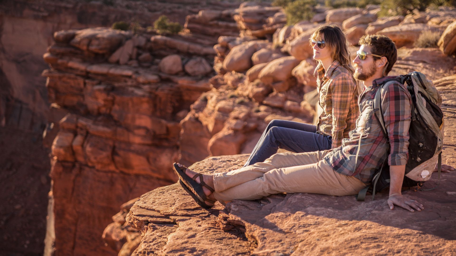 A couple sits on the edge of a canyon looking out over Canyonlands National Park and the Colorado River below