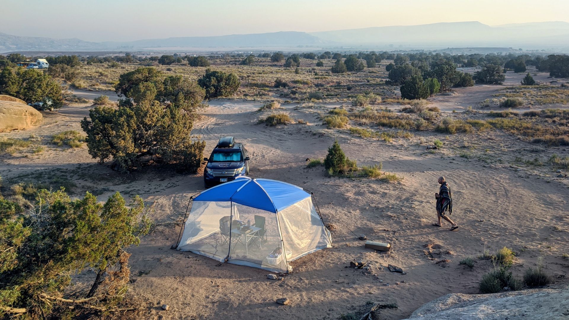 An SUV with a roof rack is parked next to a screen tent in a dispersed campsite at Utah Raptor State Park