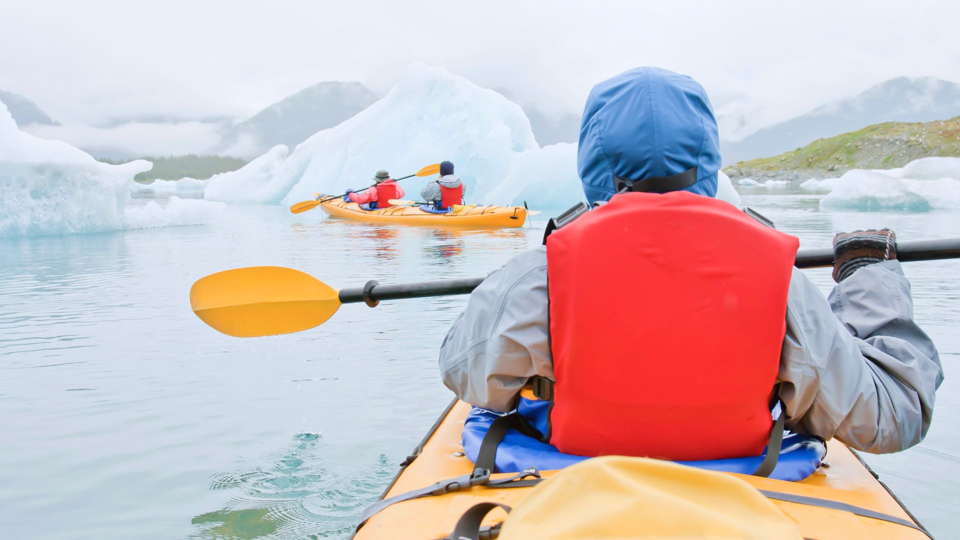 A kayaker looks ahead at a scene of icebergs and glaciers in coastal Alaska