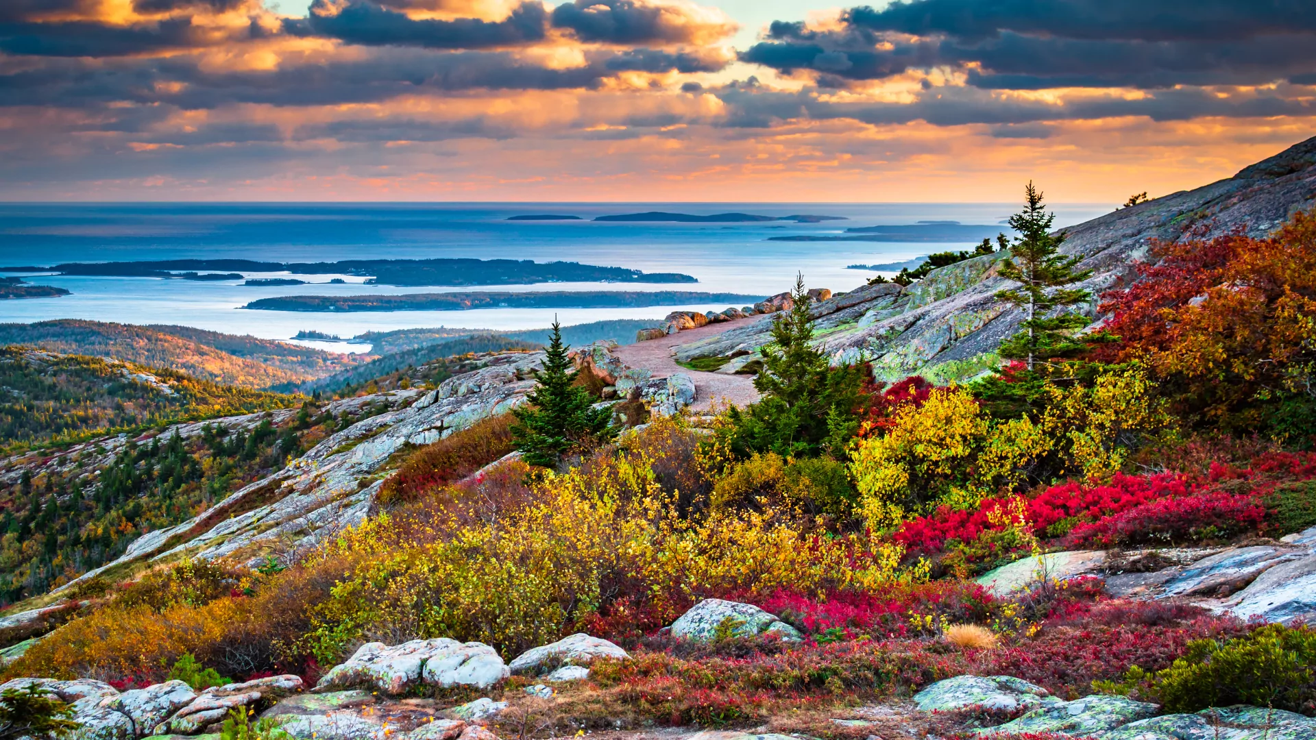 Sunrise creates colorful clouds over the Atlantic Ocean as seen from the top of a mountain covered in autumn foliage