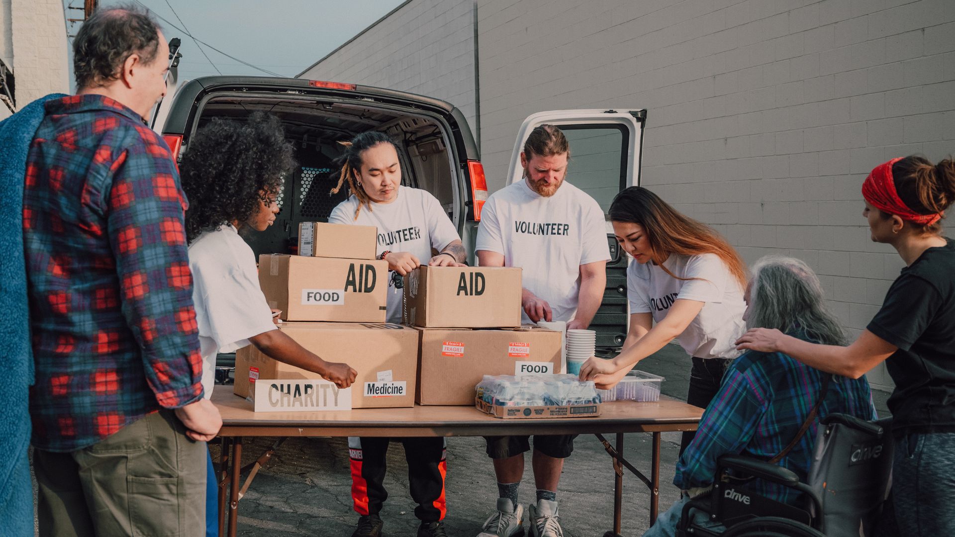 Volunteers sort boxes marked as food and medical "Aid" on a folding table as they get ready to distribute it to the waiting people nearby