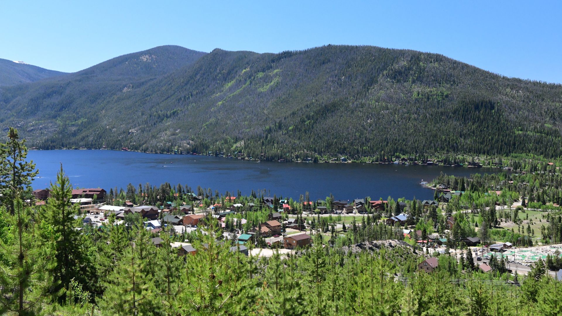 The town of Grand Lake Colorado sits alongside a lake while a forested mountain rises behind