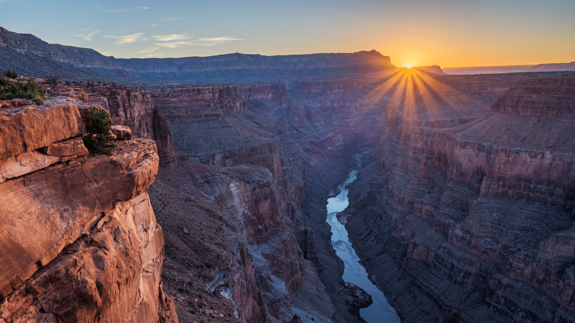 The rising sun sends rays of light shining over the south rim of the Grand Canyon as the Colorado River lies in shadow below